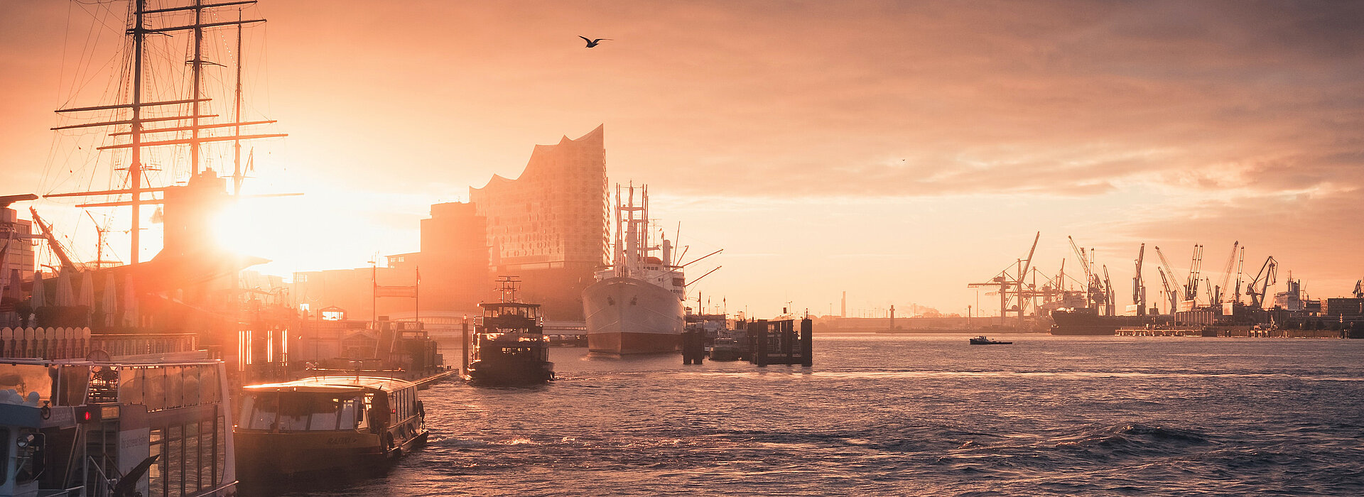 View of the Elbe in the direction of the Elbphilharmonie at sun down. The harbour and some ships are visible.