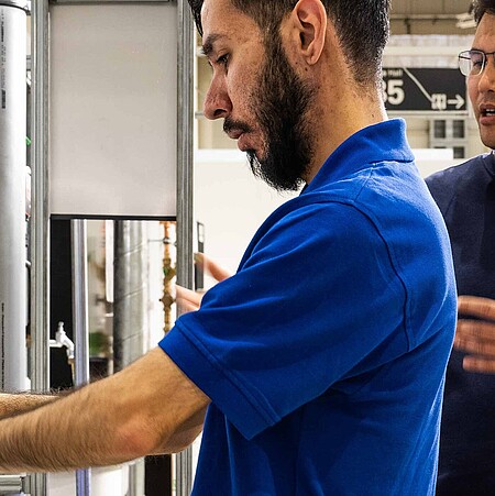 A man tests an apparatus in the TechnikPark. Another person stands behind him to explain.