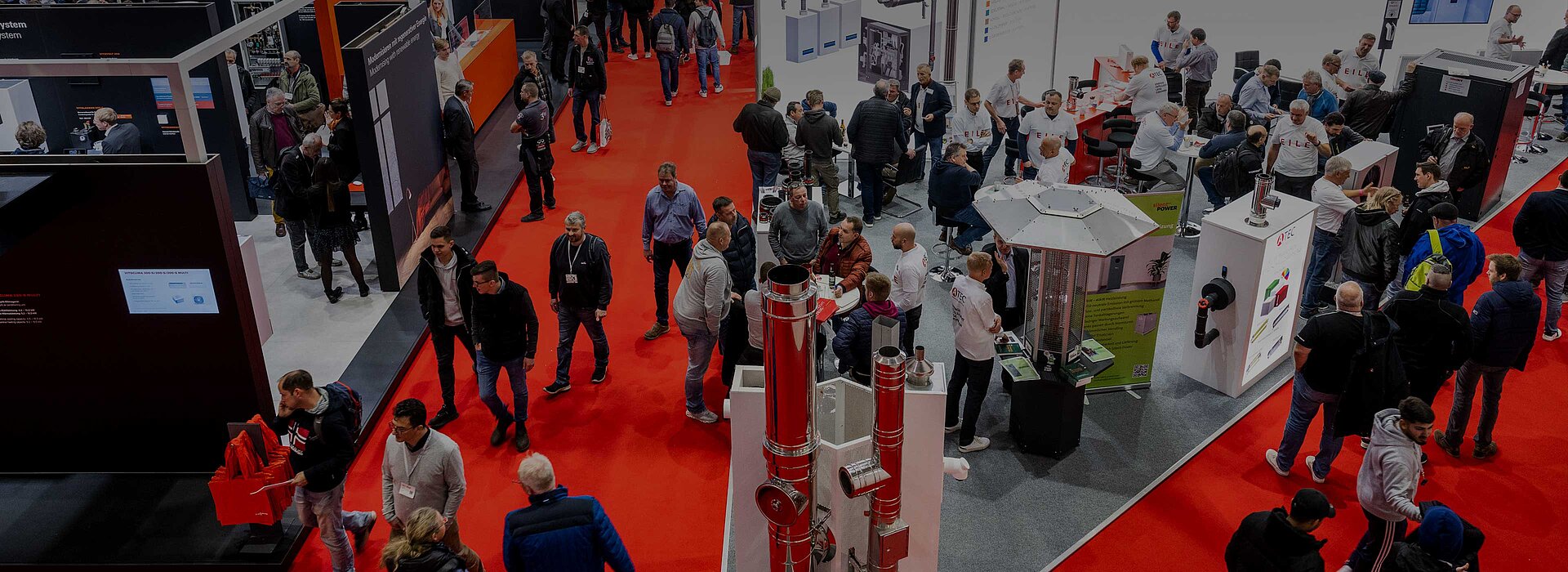 View from above of the stands in a GET NORD exhibition hall. Many people stand on the red carpets and chat.